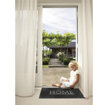 Een jong meisje zit te lezen op een deurmat met het woord 'Home' voor een open terrasdeur met uitzicht op een tuin