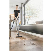 Vrouw zuigt vloeistoffen en vuil op met een nat- en droogzuiger van de houten vloer.