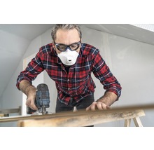 Man werkt met een decoupeerzaag, draagt een veiligheidsbril en een stofmasker.