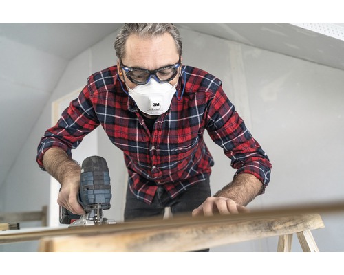 Man werkt met een decoupeerzaag, draagt een veiligheidsbril en een stofmasker.