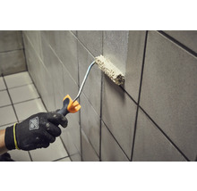 Een persoon schildert een betegelde muur met een verfroller.