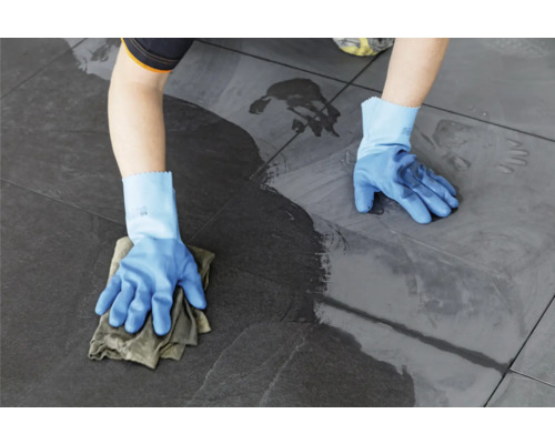 Persoon reinigt tegels met een doek en handschoenen.