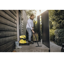 Een man maakt met een gele alleszuiger een terras voor een huis schoon.