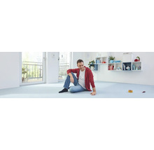 Een man zit op een lichte vloer in een lichte kamer met een balkon.