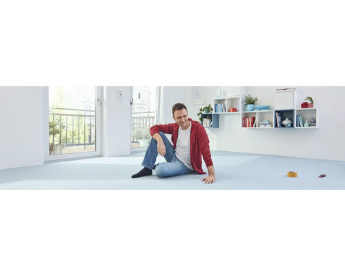 Een man zit op een lichte vloer in een lichte kamer met een balkon.