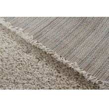 Detailopname van een beige tapijt met hoogpolig oppervlak en geweven achterkant