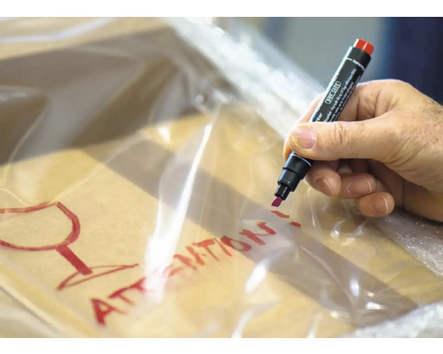 Hand beschrijft pakket met een stift en de waarschuwing breekbaar