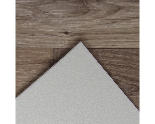 Detailopname van een witte vinyltegel op een houten vloer.