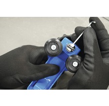 Close-up van handen met werkhandschoenen die een blauwe tegelsnijmachine afstellen met een inbussleutel.