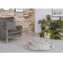 Woonkamer met grijze fauteuil, rond tapijt en kamerplanten voor een bakstenen muur.