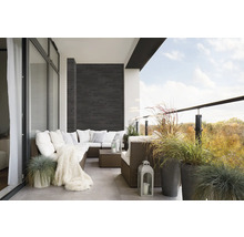 Balkon met rotan bank, kussens, deken, lantaarns en siergrassen in potten.