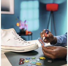 Een persoon bevestigt met lijm een embleem op een sneaker, omringd door andere emblemen op een tafel.