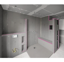 Onvoltooide badkamer met bouwplaten, douchebak en planken.