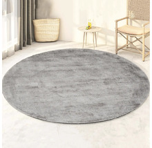 Rond grijs tapijt in de woonkamer met mand, tafel en stoel.