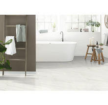Lichte badkamer met bad, handdoekladder en witte tegels in marmerlook.