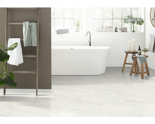 Lichte badkamer met bad, handdoekladder en witte tegels in marmerlook.
