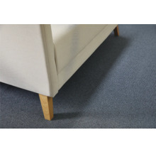 Detail van gestoffeerd meubel met stoffen bekleding en houten poten op een tapijtvloer.