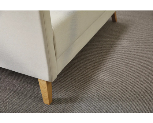 Detailweergave van een gestoffeerde fauteuil met houten poten op een tapijt