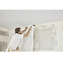 Man op ladder bevestigt behang aan de muur