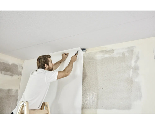 Man op ladder bevestigt behang aan de muur