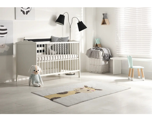 Lichte kinderkamer met ledikant, staande lamp, kinderstoel en vloerkleed met diermotief