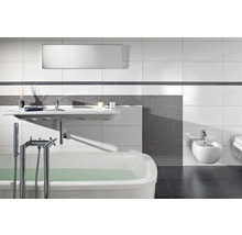 Moderne badkamer met wit ligbad, wandwastafel en bidet, grijze mozaïektegels en grote witte wandtegels.