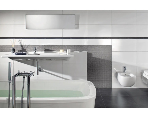 Moderne badkamer met wit ligbad, wandwastafel en bidet, grijze mozaïektegels en grote witte wandtegels.