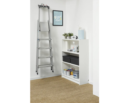 Georganiseerde opslagruimte met een witte stellingkast en een aluminium trapladder aan de muur. De kast bevat verf en opbergdozen.
