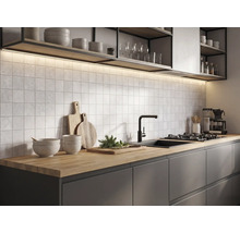 Moderne keuken met houten werkblad, donkere kasten, vierkante wandtegels, zwarte kraan en verlichting onder de planken.
