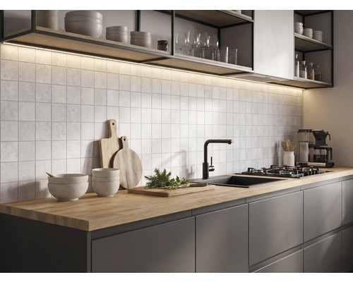 Moderne keuken met houten werkblad, donkere kasten, vierkante wandtegels, zwarte kraan en verlichting onder de planken.