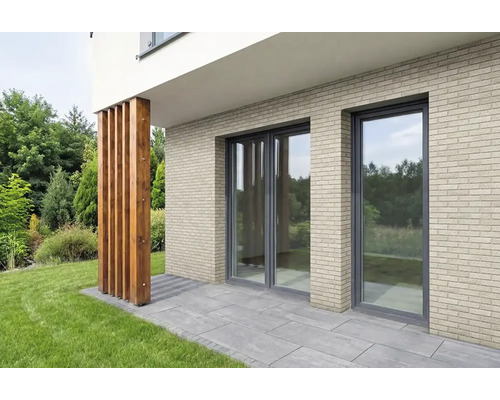 Gevel met lichtbeige steenstrips in baksteenlook, kamerhoge ramen en een terras met grijze stenen tegels.