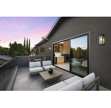 Modern dakterras met grijze bakstenen gevel, glazen schuifdeur, loungemeubels en glazen balustrade.