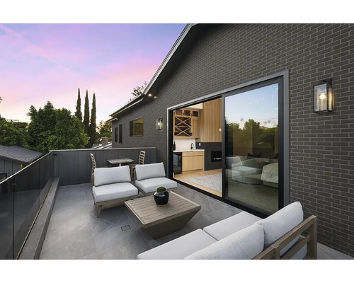 Modern dakterras met grijze bakstenen gevel, glazen schuifdeur, loungemeubels en glazen balustrade.
