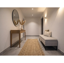 Lichte hal met houten sidetable, ronde spiegel, jute loper en gestoffeerde bank. Modern, minimalistisch ontwerp met warme verlichting.