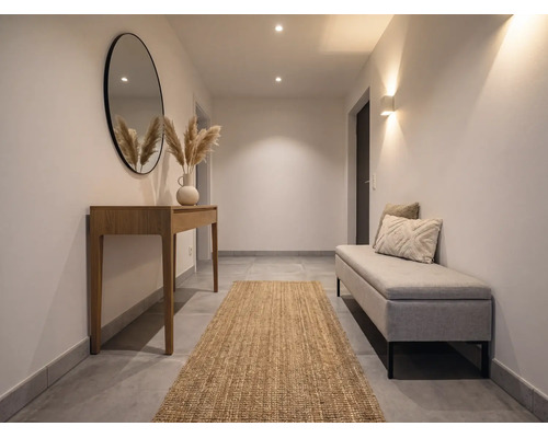 Lichte hal met houten sidetable, ronde spiegel, jute loper en gestoffeerde bank. Modern, minimalistisch ontwerp met warme verlichting.