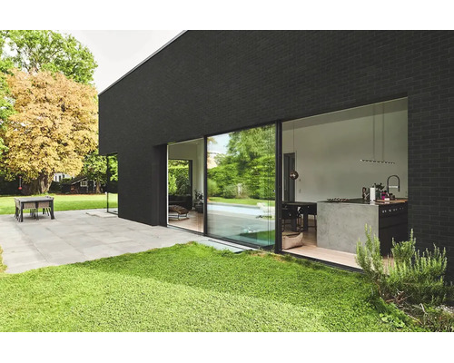 Moderne gevel met grote glazen schuifdeur, zicht op de keuken, een terras met stenen tegels en een gazon.
