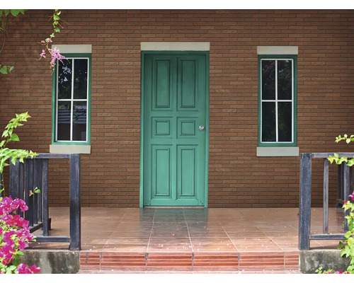 Bakstenen gevel van een huis met een groene deur, twee ramen en een betegeld terras.