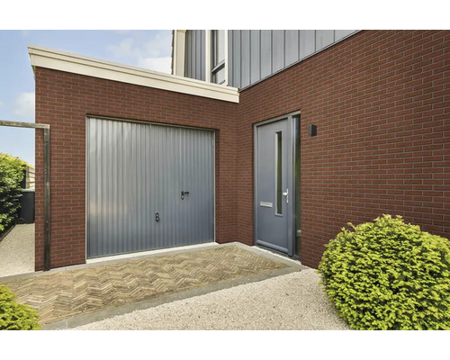Buitengevel van een woning met steenstrips, grijze garagedeur, moderne voordeur en bestrate entree.
