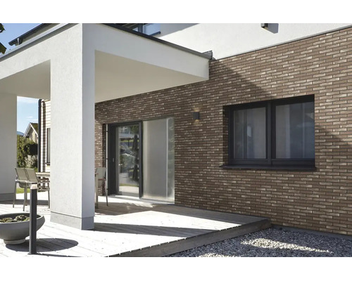 Moderne gevel met bruine steenstrips bij een terras met houten vlonder en witte kolommen.