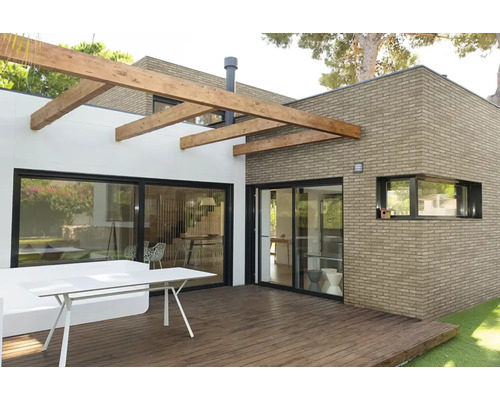 Modern terras met houten vlonder, bakstenen gevel en pergola van houten balken.