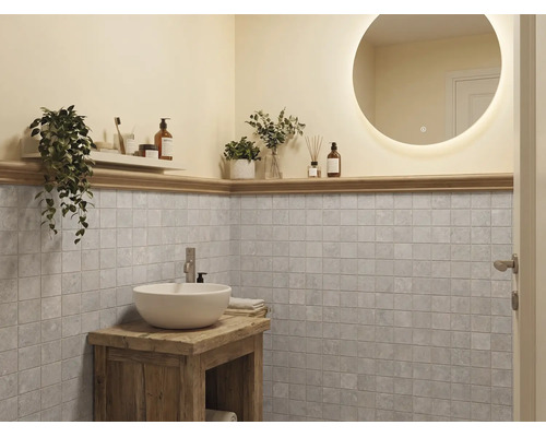 Moderne badkamer met ronde verlichte spiegel, witte waskom op rustiek houten meubel en grijze vierkante wandtegels.