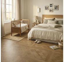 Lichte slaapkamer met een decoratieve parketvloer met patroon, een houten bed met licht beddengoed en een houten babybedje bij het raam.