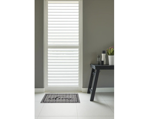 Deurmat met het opschrift Welcome voor een raam met witte shutters in een lichte, moderne hal.
