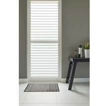 Witte houten shutters voor een raam tegen een grijze muur met een grijze deurmat met de tekst home op een lichte tegelvloer.