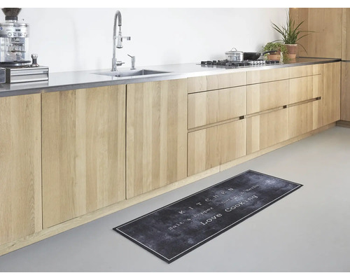 Moderne keukenloper met tekst Love Cooking in een lichte keuken met houten kasten en rvs aanrechtblad.