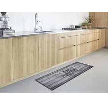 Moderne keuken met lichte houten kasten en een keukenloper met houtmotief en de tekst Bon Appetit op de vloer.
