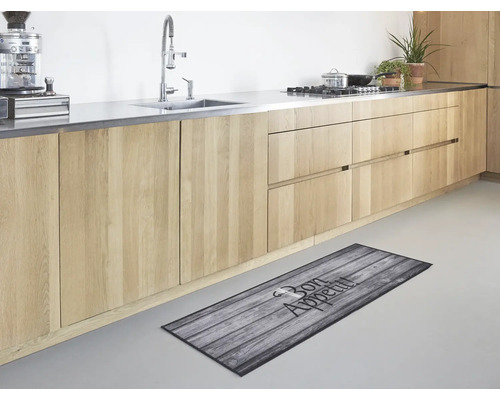 Moderne keuken met lichte houten kasten en een keukenloper met houtmotief en de tekst Bon Appetit op de vloer.