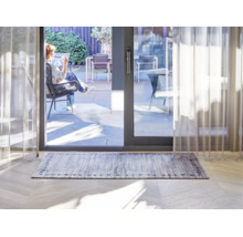 Rechthoekig vloerkleed met grijs houtplankenpatroon en decoratieve rand in een lichte woonkamer voor een schuifpui naar het terras.