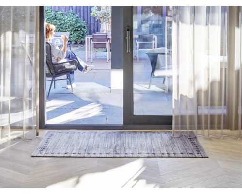 Rechthoekig vloerkleed met grijs houtplankenpatroon en decoratieve rand in een lichte woonkamer voor een schuifpui naar het terras.