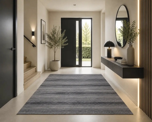 Moderne entree met een grijs vloerkleed, houten trap, zwarte deur en een zwevend consolemeubel met spiegel.